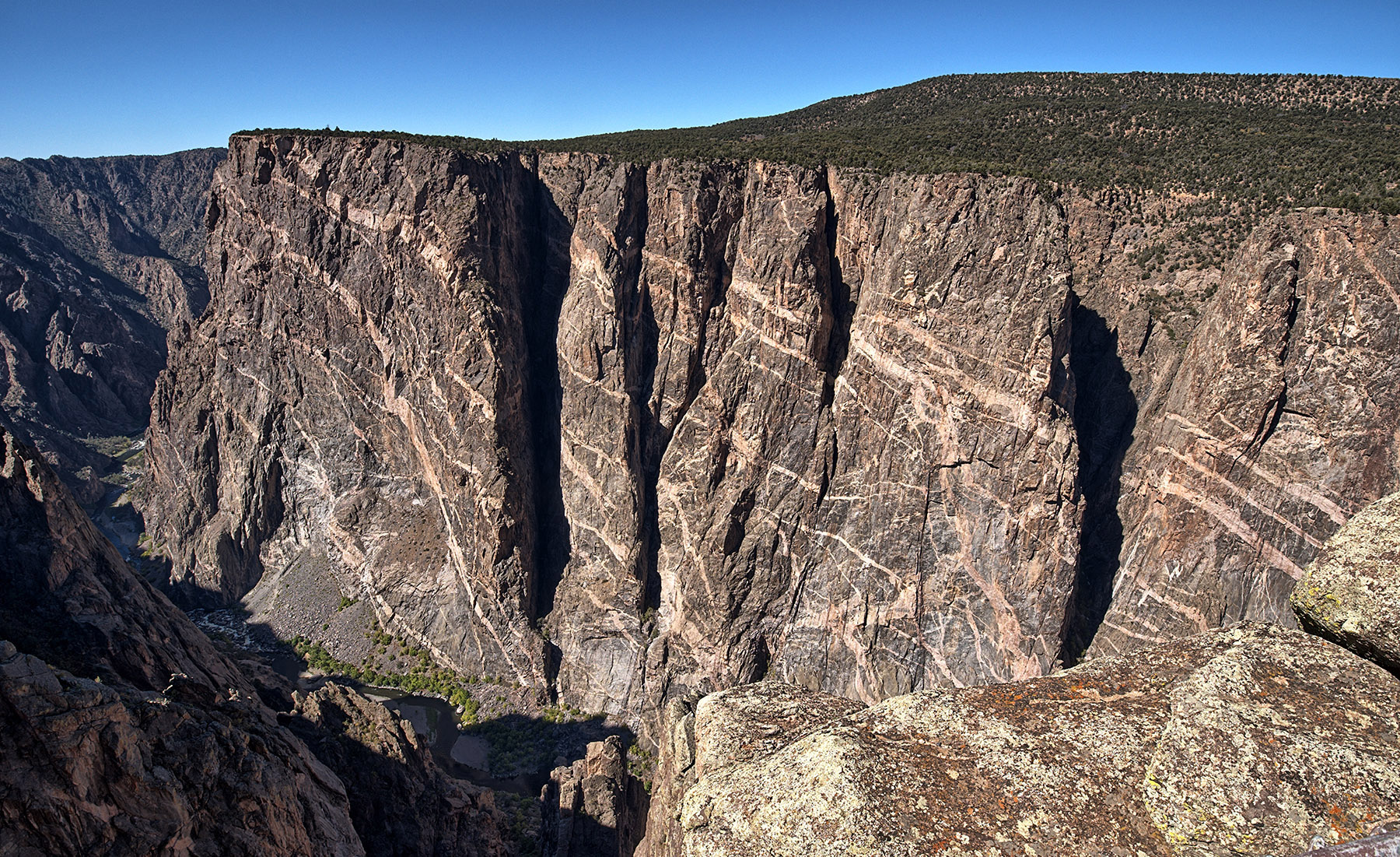 2300 foot Painted Wall, Black Canyon of the Gunnison.  1800 Ma gneiss was penetrated by veins of pegmatite powered by a 1,400 Ma intrusion of granite pushing hot fluids rich in feldspar and quartz that crystallized as it cooled to form pegmatite.