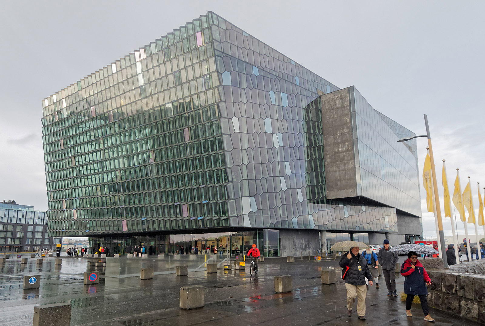 Harpa Reykjavik Concert Hall and Conference Center and tourists.   Only tourists carry umbrellas in Iceland (Think what happens to umbrellas in regularly occurring wind gusts of 30-40 mph!).