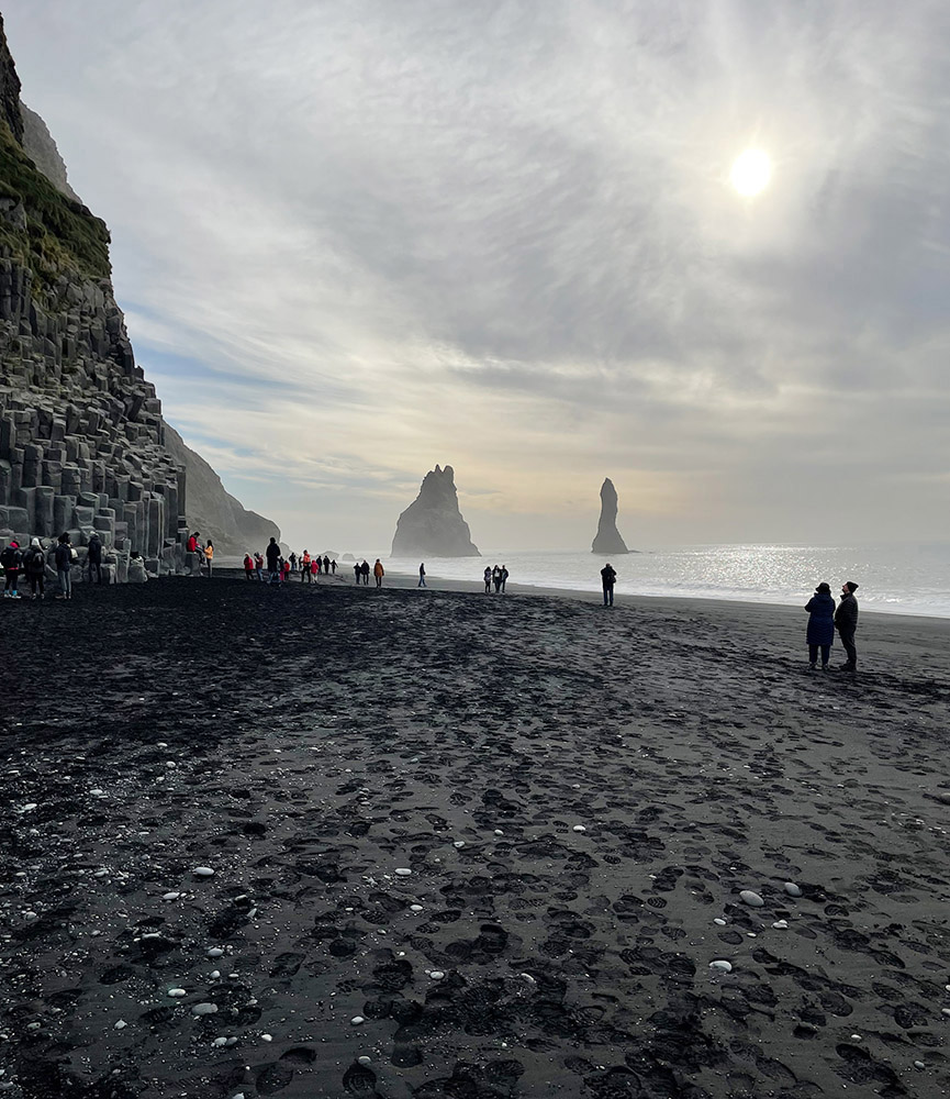 Black sand beach at Reynisfjara. Columnar basalt to left, fine black sand produced by erosion and ocean action on basalt, and sea rock pillars composed of eroded basalt in the water. Photo by Joan Castleman.