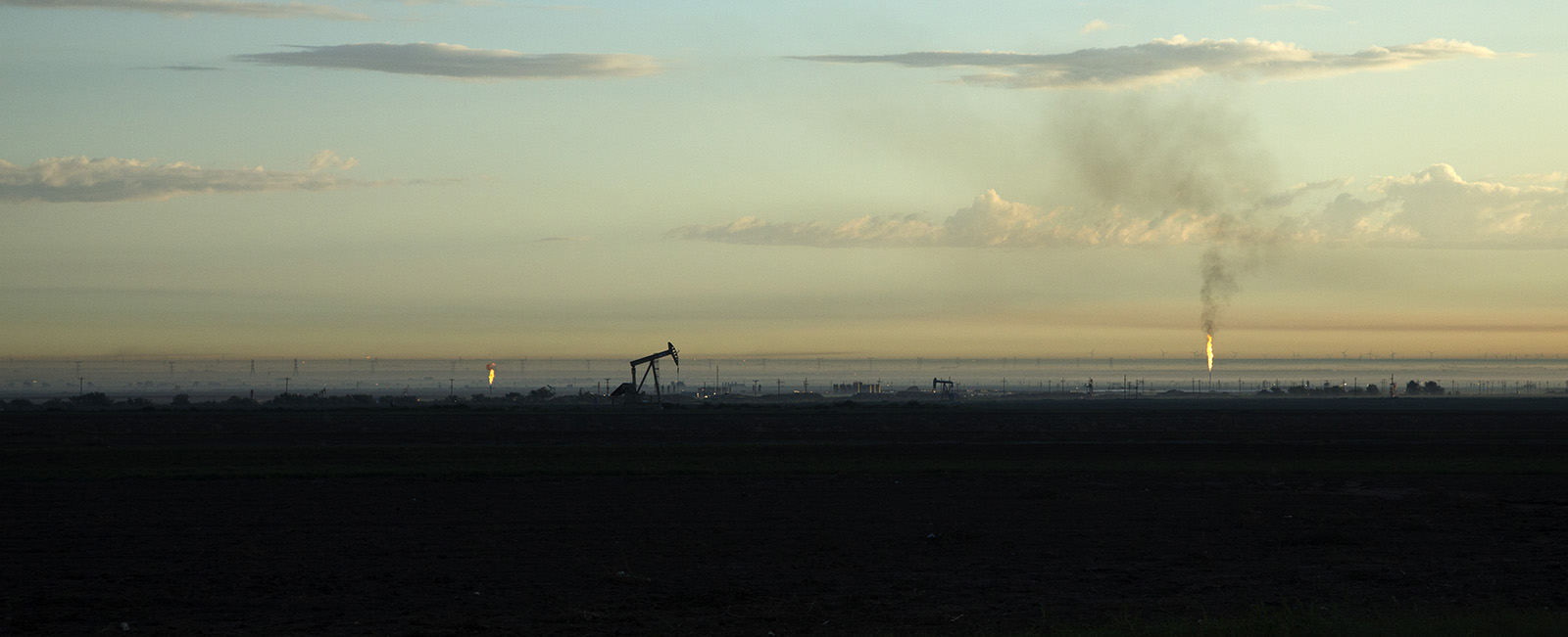 Midland Basin sunrise with oil pump jacks and natural gas flares contributing to ground haze in early morning.