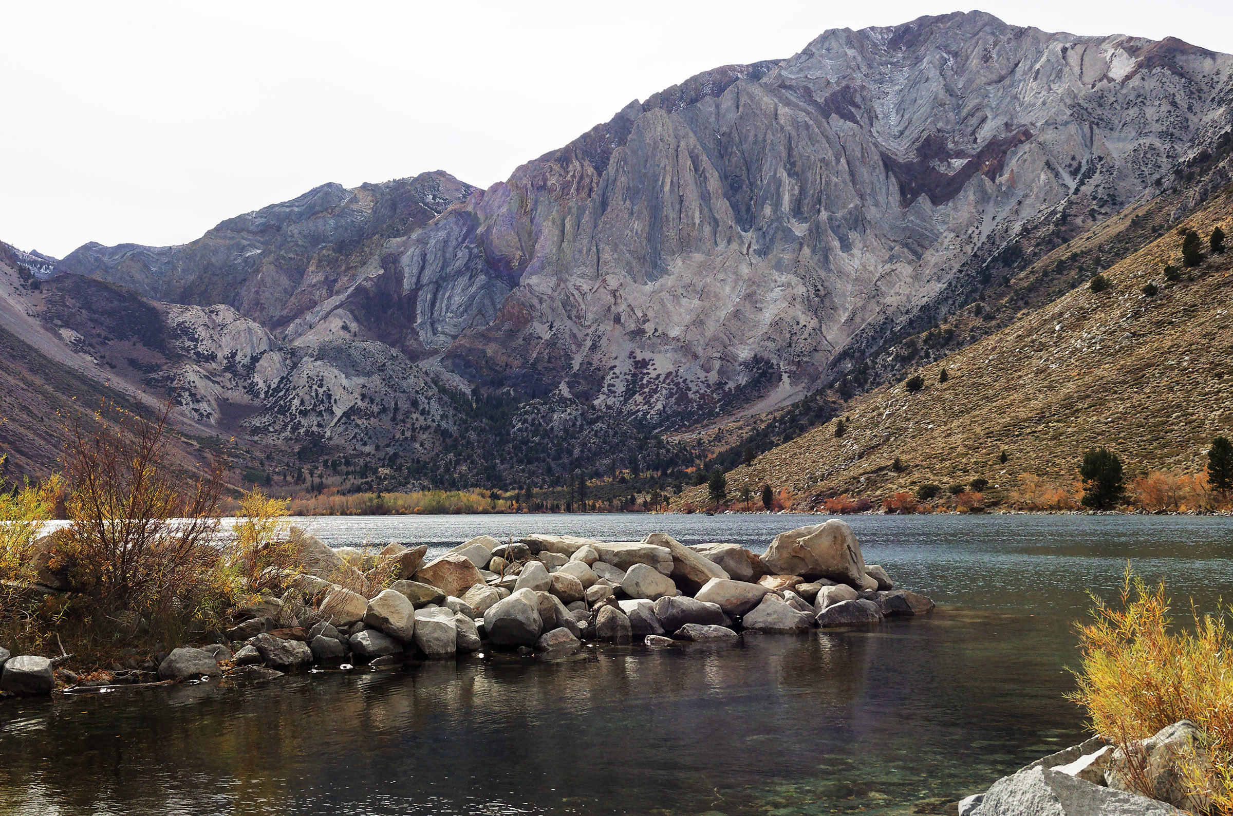 Western edge of Convict Lake showing Laurel Mountain (highest peak) and Sevehah Cliff.  Laurel Mountain and Sevehah Cliff are part of the roof pendant of Paleozoic metasedimentary rock that was raised and compressed by injected underlying molten magma that formed the Sierra Nevada batholith.