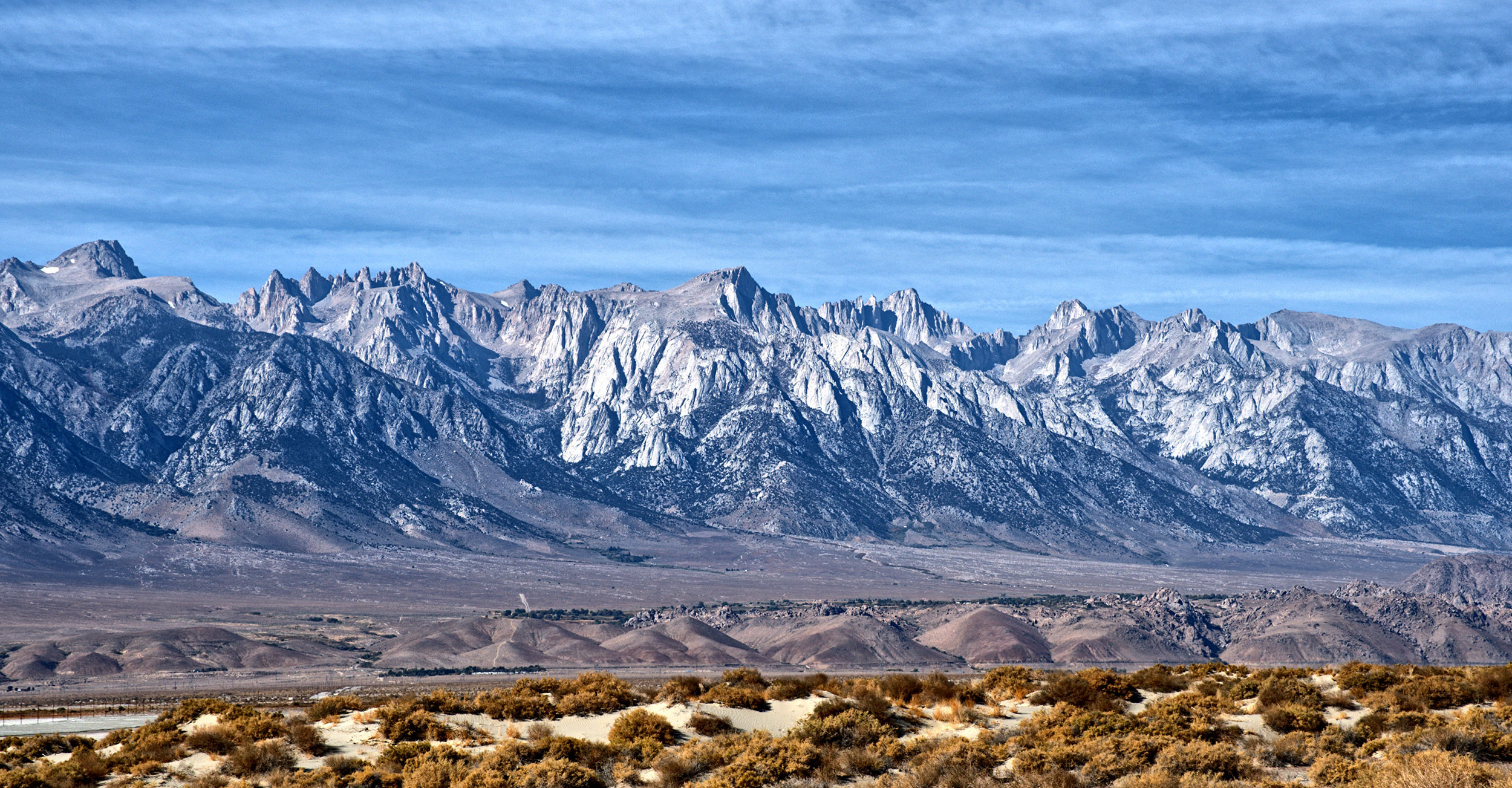 Eastern face of the Sierra Nevada Mountains with Alabama Hills in the foreground.  Exposed granite mountain peaks eroded by glacial action represent the batholith that was formed when the Farallon Plate subducted beneath North American Plate and resulting magma rose from 20 to 60 miles beneath the crust over 225 to 80 Ma to form the plutonic rocks (granite) beneath the surface.  This batholith was lifted abruptly along the Sierra Nevada fault and eroded by glacial activity over the last 2 million years to form the jagged granite peaks we see today.